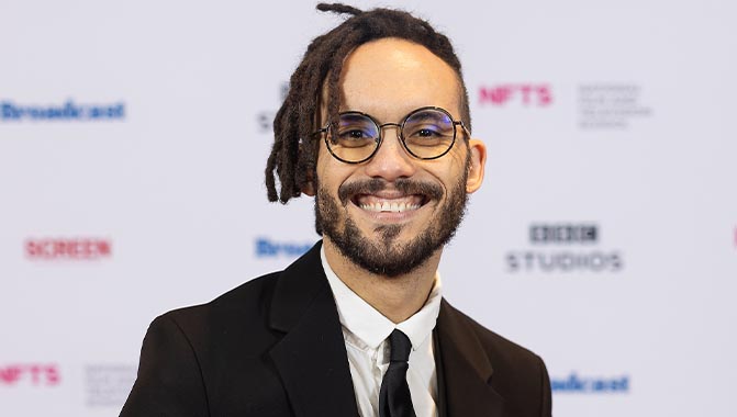 Young man with glasses and facial hair standing in front a background with logos